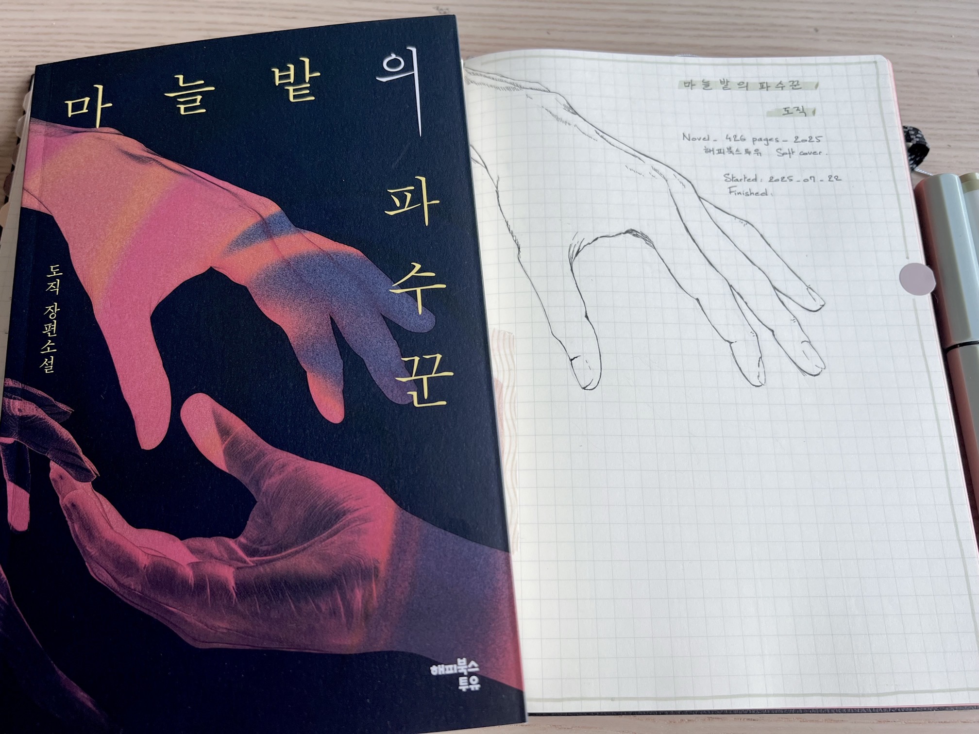 A book with two hands reaching towards one another, one facing down and the other facing up + a notebook with the hand facing down drawn with a pen.