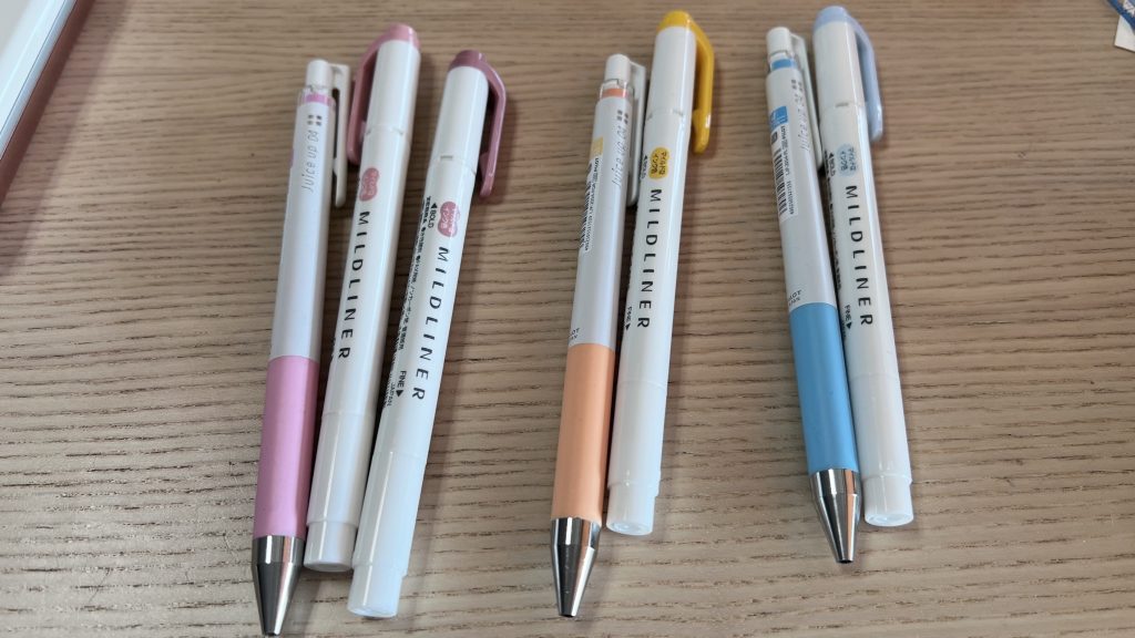 7 pens and markers on a table grouped by colours: pink, orange and blue.