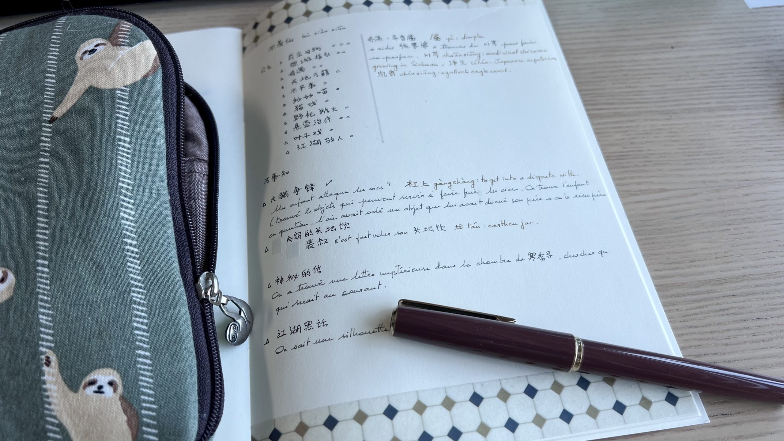 Notebook opened so that the right page is displayed. The page contains notes in Chinese and French. A fountain pen is on the page and a fabric pouch is resting on the left page of the notebook.